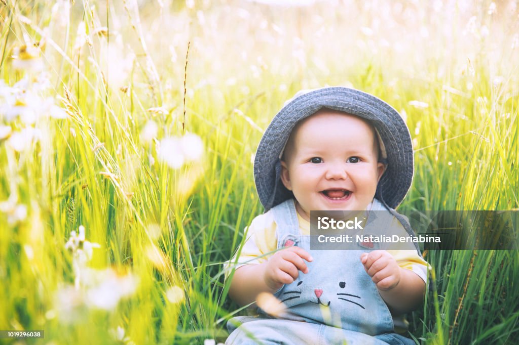 Baby in nature. Cutest smiling little girl in green grass with flowers at summertime. Image of childhood. Parents and activity with kid outdoors. Beautiful happy child sits on meadow in the park.