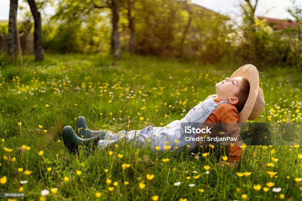 Cute little boy sitting in the grass and enjoying a carefree spring day in nature.