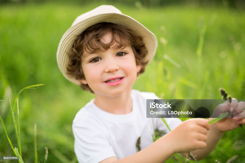 A Portrait of adorable kid boy with hat standing on a summer meadow